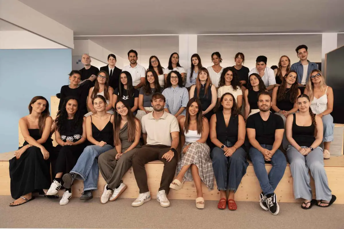 Grupo numeroso de personas jóvenes posando sonriendo en varios niveles de gradas de madera dentro de una oficina luminosa Grupo numeroso de personas jóvenes posando sonriendo en varios niveles de gradas de madera dentro de una oficina luminosa
