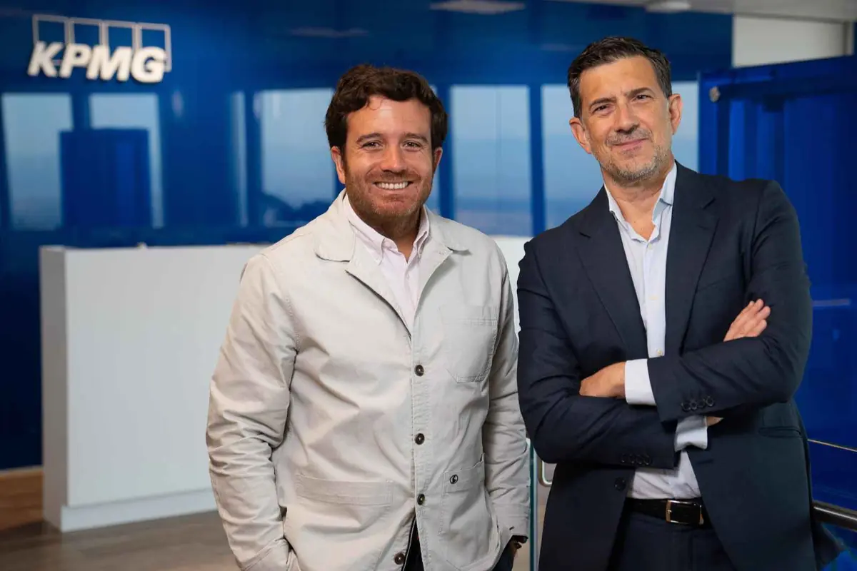 Dos hombres sonrientes con ropa de negocios posan en la recepción de una oficina moderna con el logotipo de KPMG al fondo Dos hombres sonrientes con ropa de negocios posan en la recepción de una oficina moderna con el logotipo de KPMG al fondo