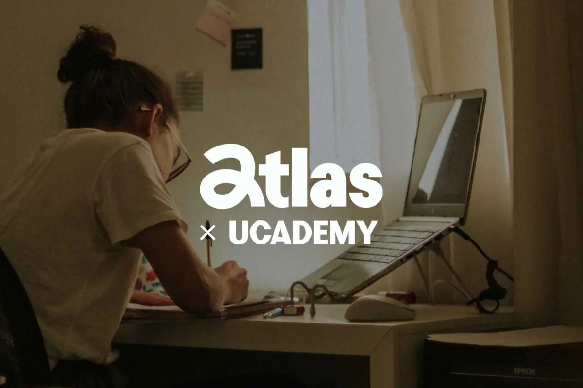 Persona estudiando en un escritorio frente a un portátil con el logotipo de la colaboración Atlas x Ucademy superpuesto en el centro de la imagen Persona estudiando en un escritorio frente a un portátil con el logotipo de la colaboración Atlas x Ucademy superpuesto en el centro de la imagen