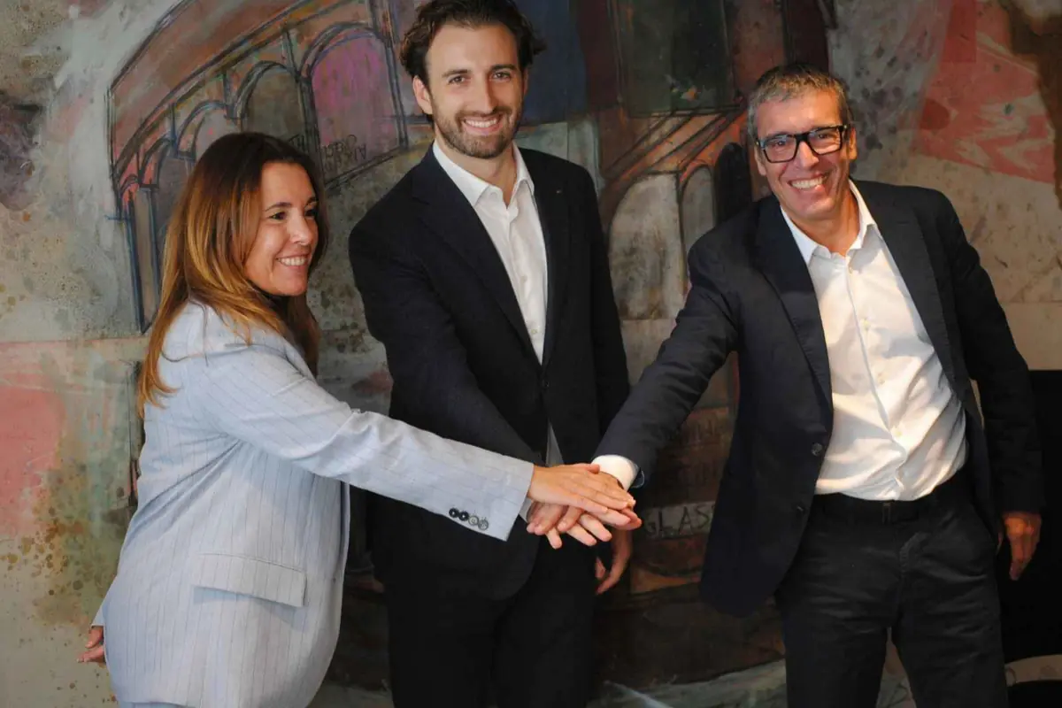 Tres personas con traje sonriendo y apilando sus manos al frente en gesto de acuerdo profesional Tres personas con traje sonriendo y apilando sus manos al frente en gesto de acuerdo profesional