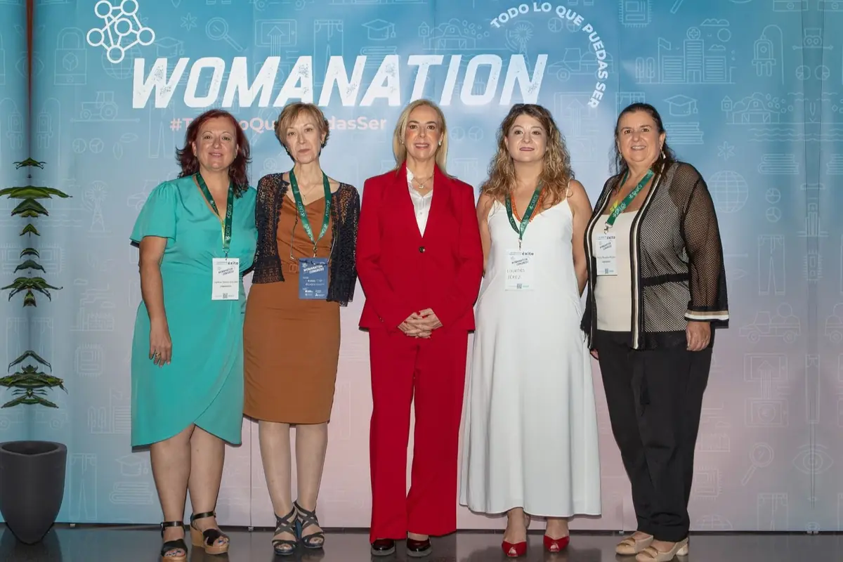 Cinco mujeres posan sonrientes frente a un fondo del evento Womanation con acreditaciones colgadas del cuello