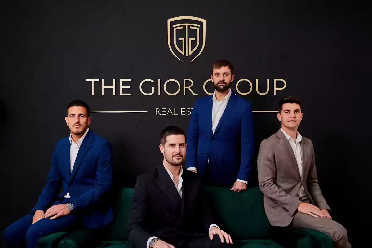 Cuatro hombres en trajes formales posan frente a un fondo negro con el logotipo de "The Gior Group Real Estate".