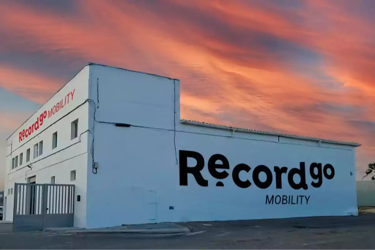 Edificio blanco con el logo de "Record go Mobility" en la fachada bajo un cielo con nubes rosadas al atardecer.