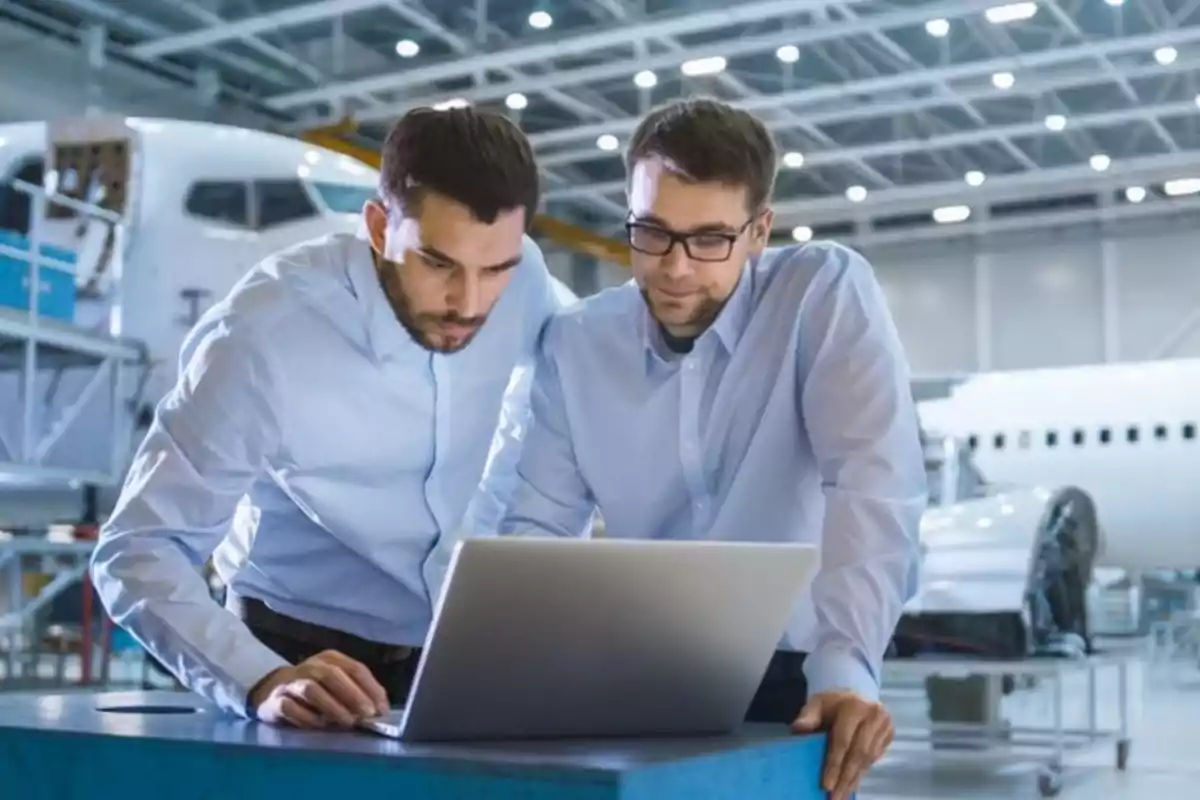 Dos hombres trabajando en una computadora portátil en un hangar de aviones.