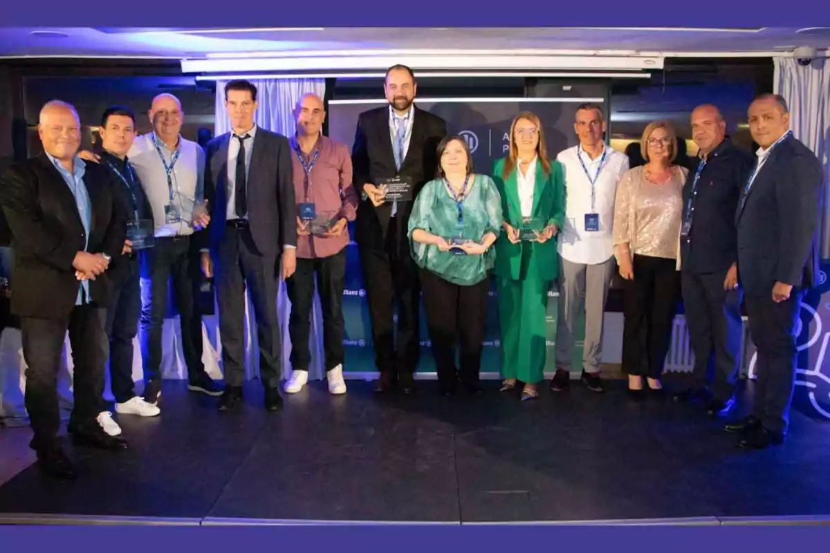 Un grupo de personas posando en un escenario, algunas sosteniendo trofeos, con un fondo azul y cortinas blancas.