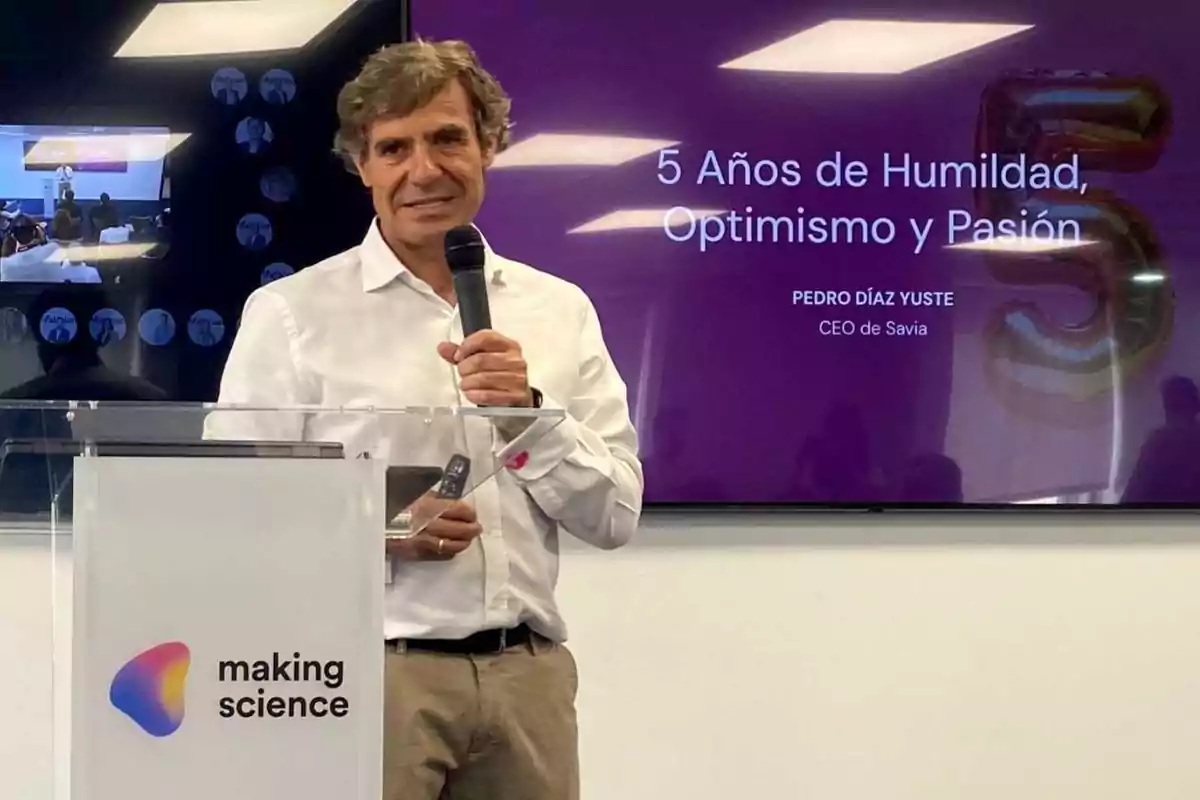 Un hombre con camisa blanca está hablando en un micrófono en un evento de "making science" con un cartel detrás que dice "5 Años de Humildad, Optimismo y Pasión" y "PEDRO DÍAZ YUSTE CEO de Savia".