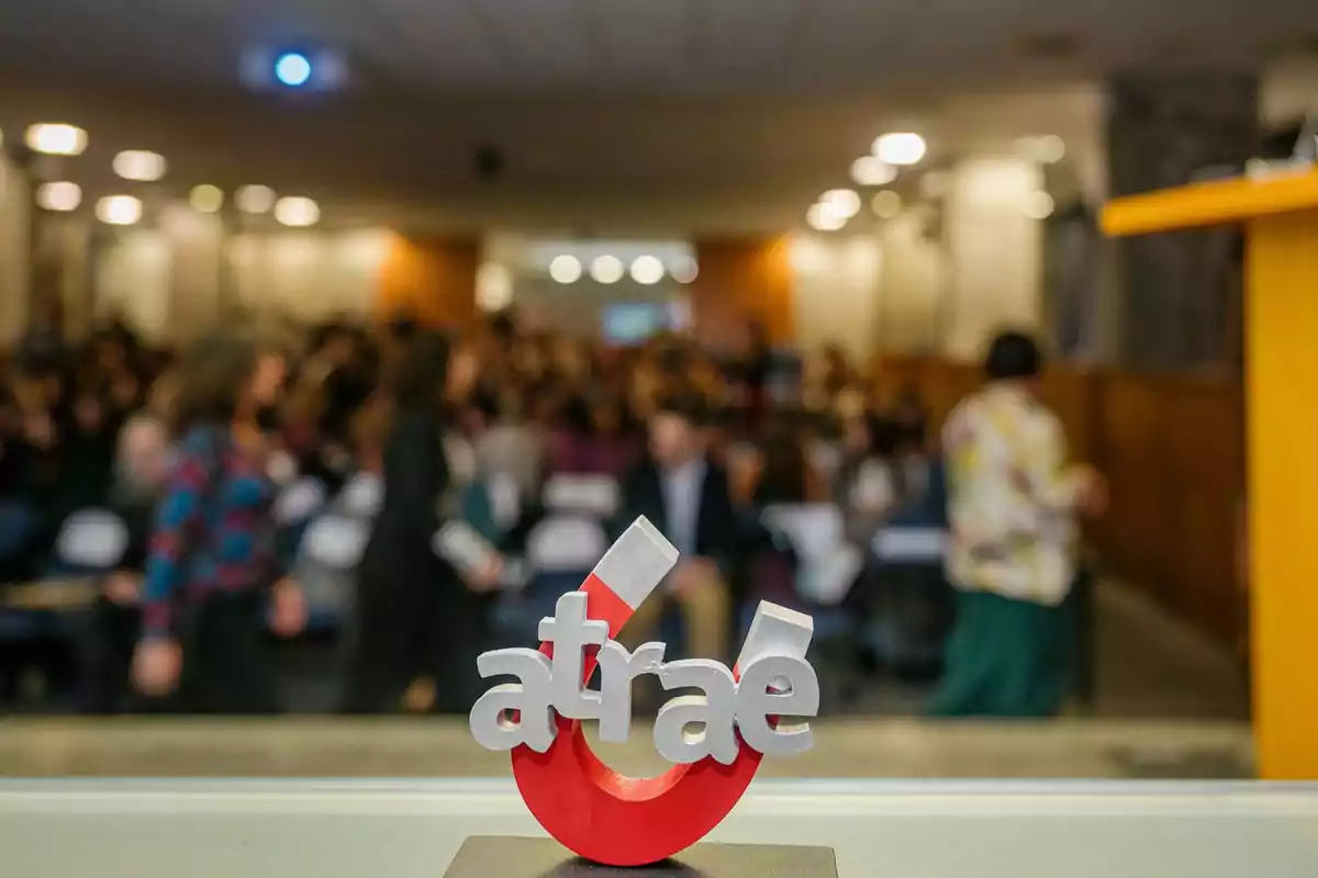 Un trofeo con la palabra "atrae" en primer plano con un fondo desenfocado de personas en un auditorio.