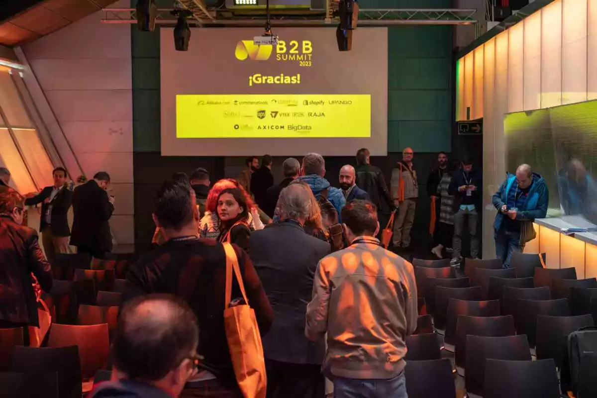 Personas reunidas en un evento de negocios con una pantalla que muestra "B2B Summit 2023 ¡Gracias!" y varios logotipos de empresas.