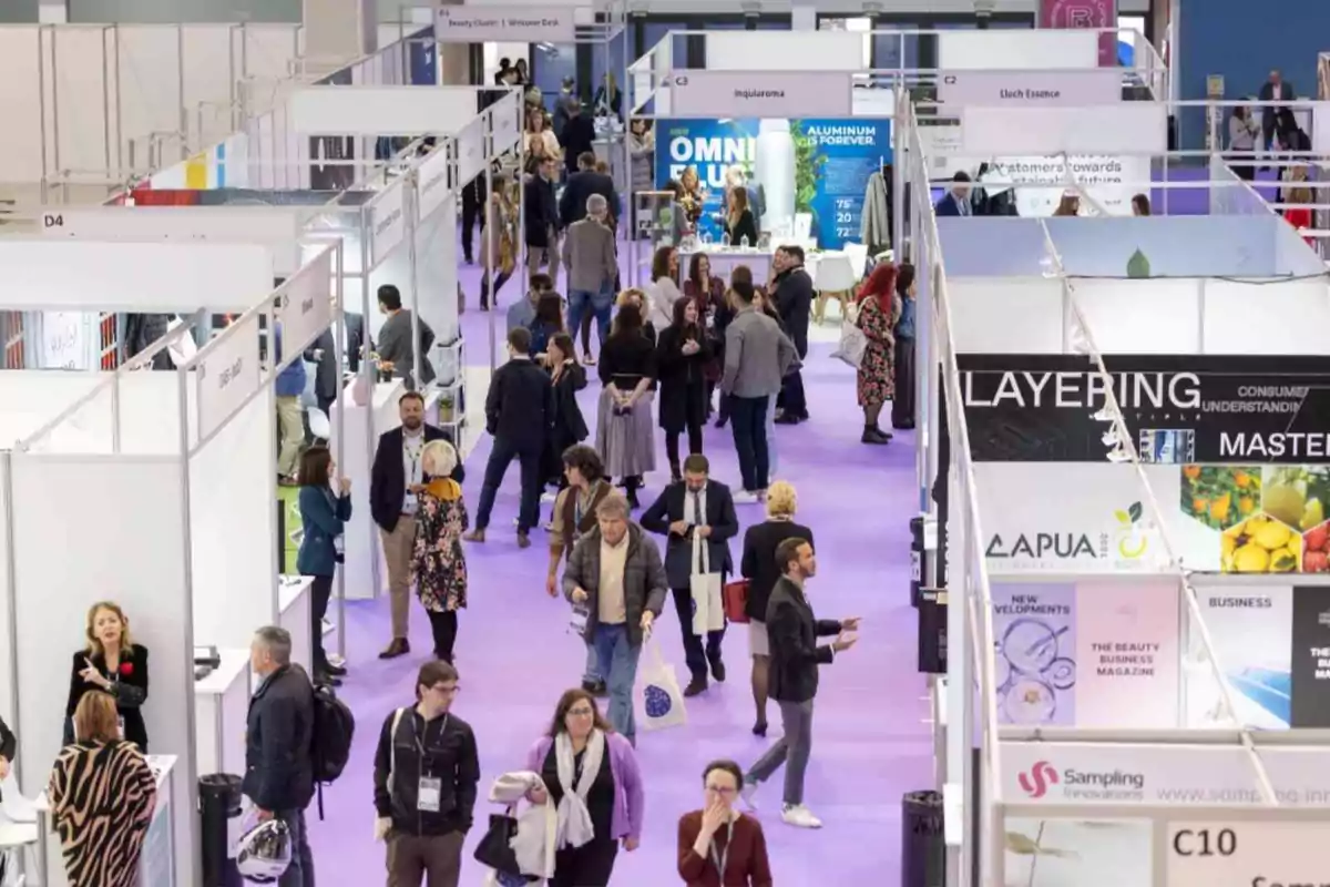 Personas caminando y conversando en un pasillo de una feria comercial con varios stands y carteles de diferentes empresas