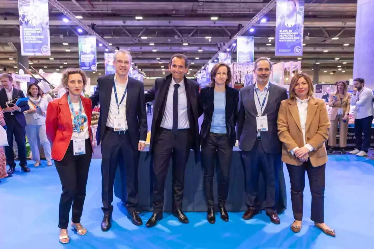 Un grupo de personas posando en un evento o conferencia en un recinto con iluminación azul y carteles colgantes.