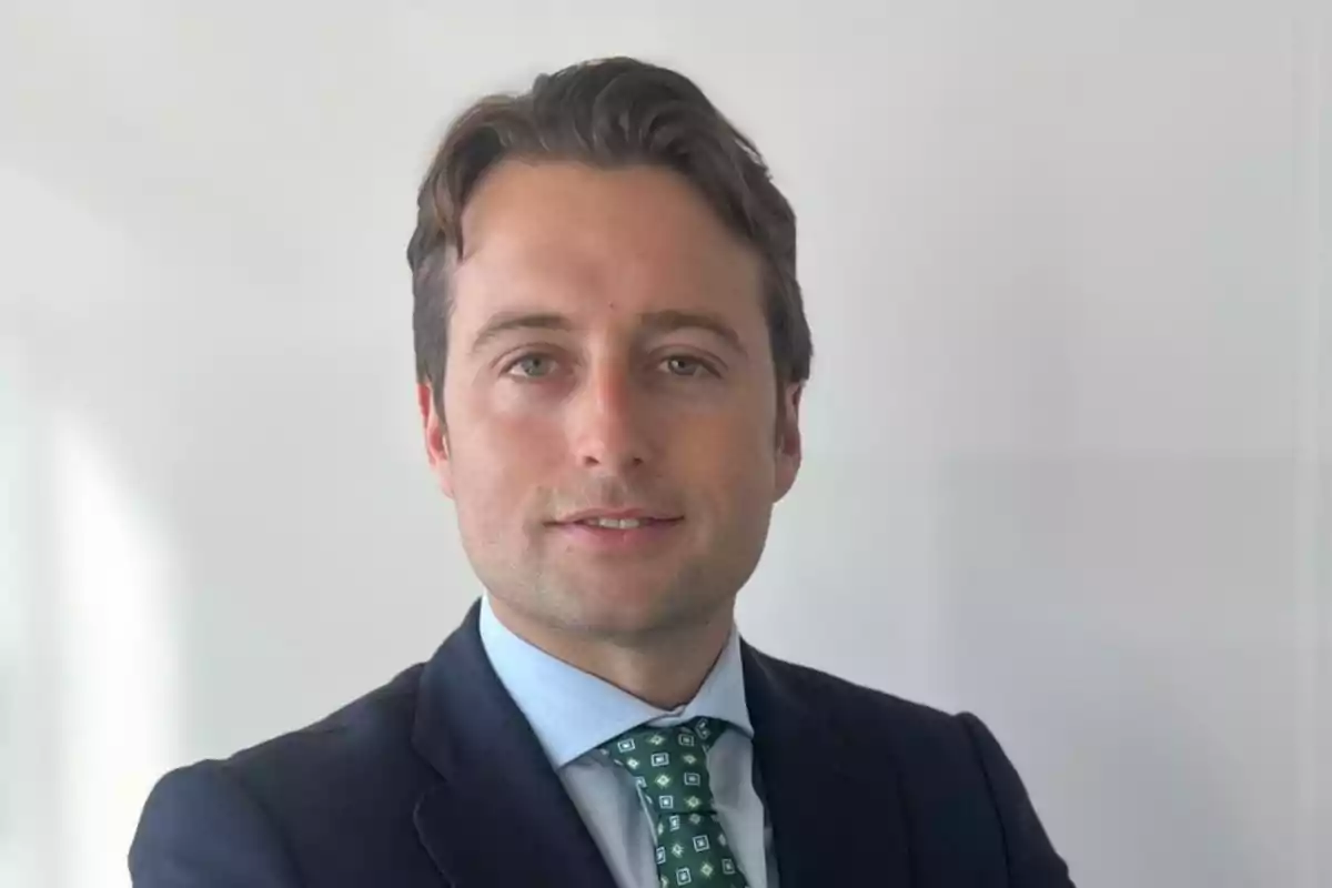 Hombre joven con cabello castaño y traje oscuro posando frente a un fondo claro