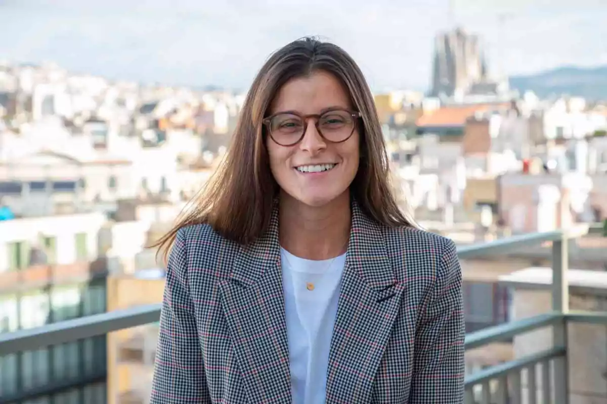 Una persona con gafas sonriendo en una terraza con una ciudad de fondo.