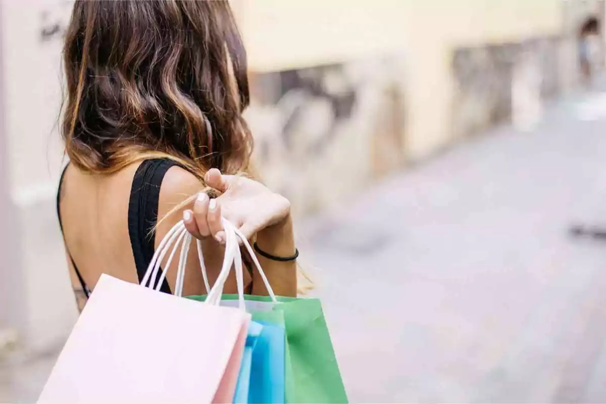 Mujer de espaldas sosteniendo bolsas de compras de colores en una calle peatonal.