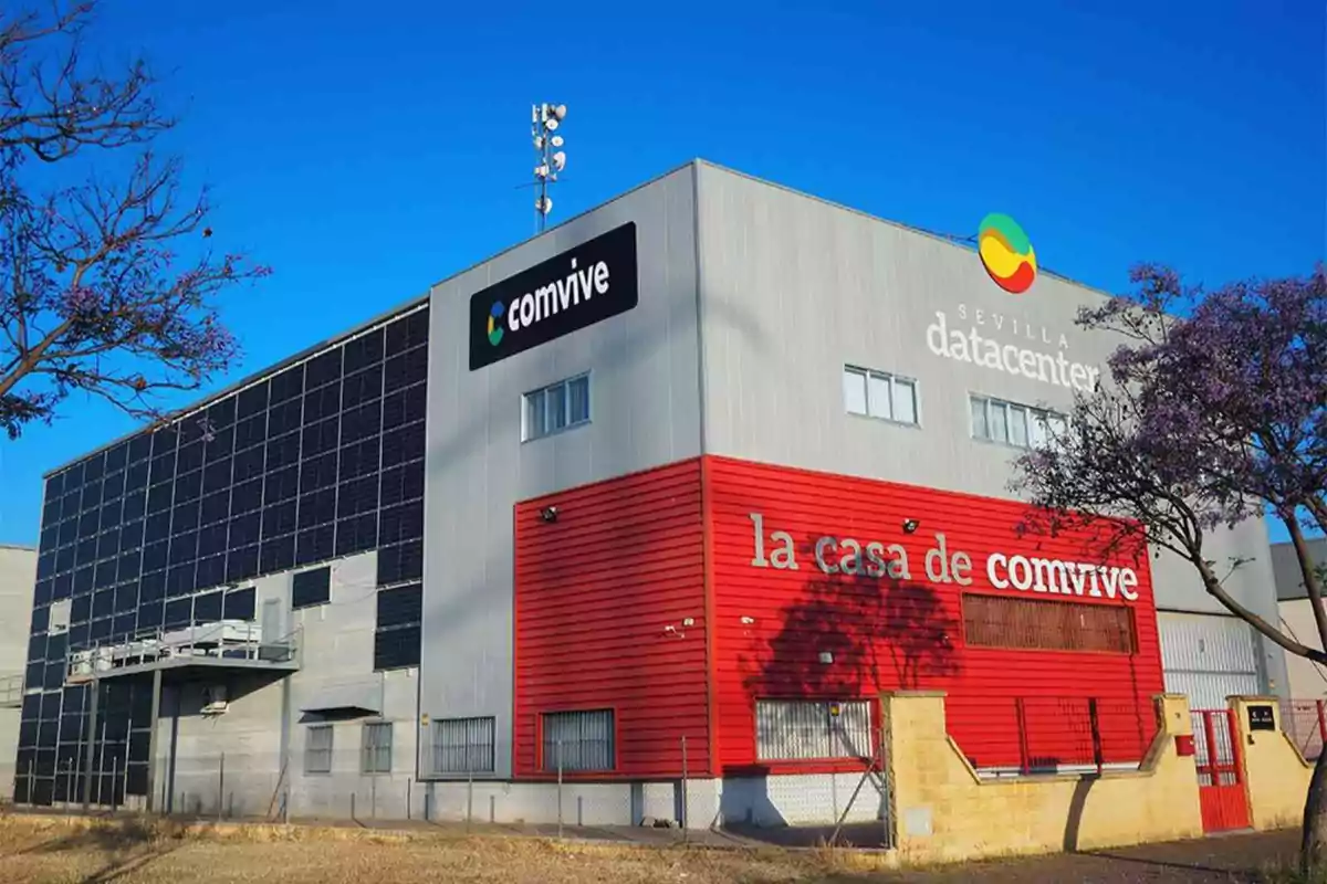 Edificio moderno con paneles solares en la fachada y letreros que indican Sevilla datacenter y la casa de comvive bajo un cielo azul despejado