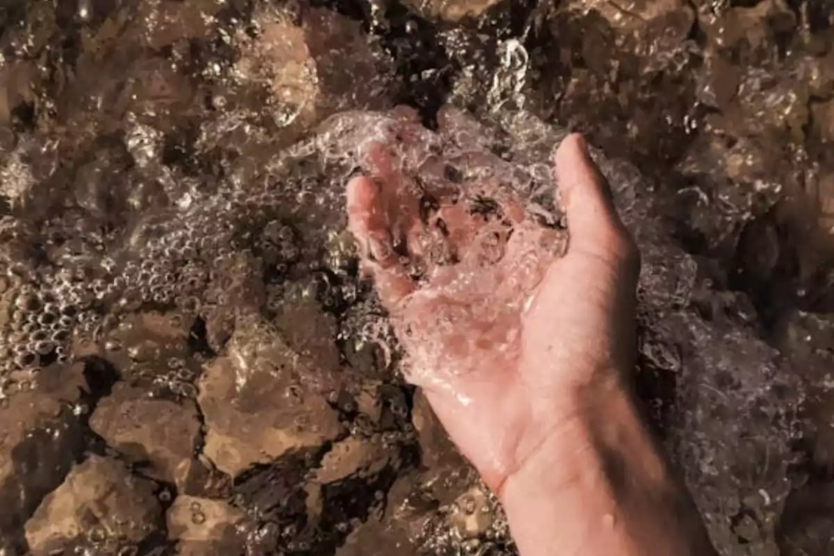 Una mano sumergida en agua clara sobre un fondo de piedras.