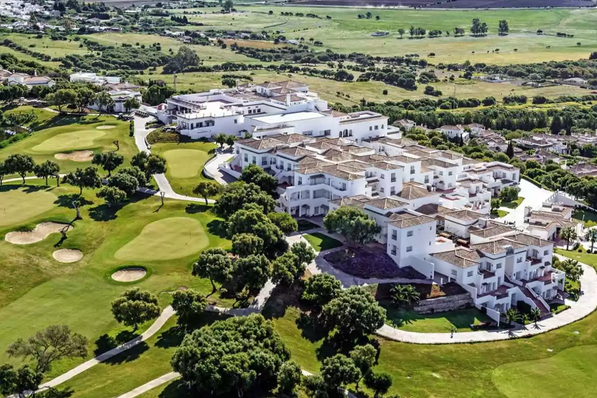 Vista aérea de un complejo residencial rodeado de un campo de golf con áreas verdes y caminos pavimentados.