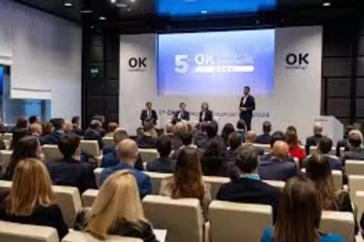 Personas asistiendo a una conferencia en un auditorio con un panel de oradores al frente.