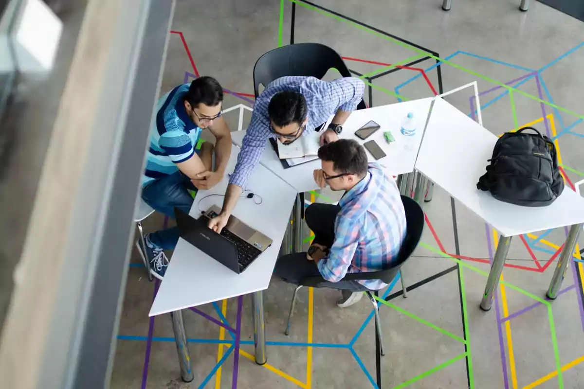 Tres personas trabajando en una mesa con una computadora portátil y teléfonos móviles.