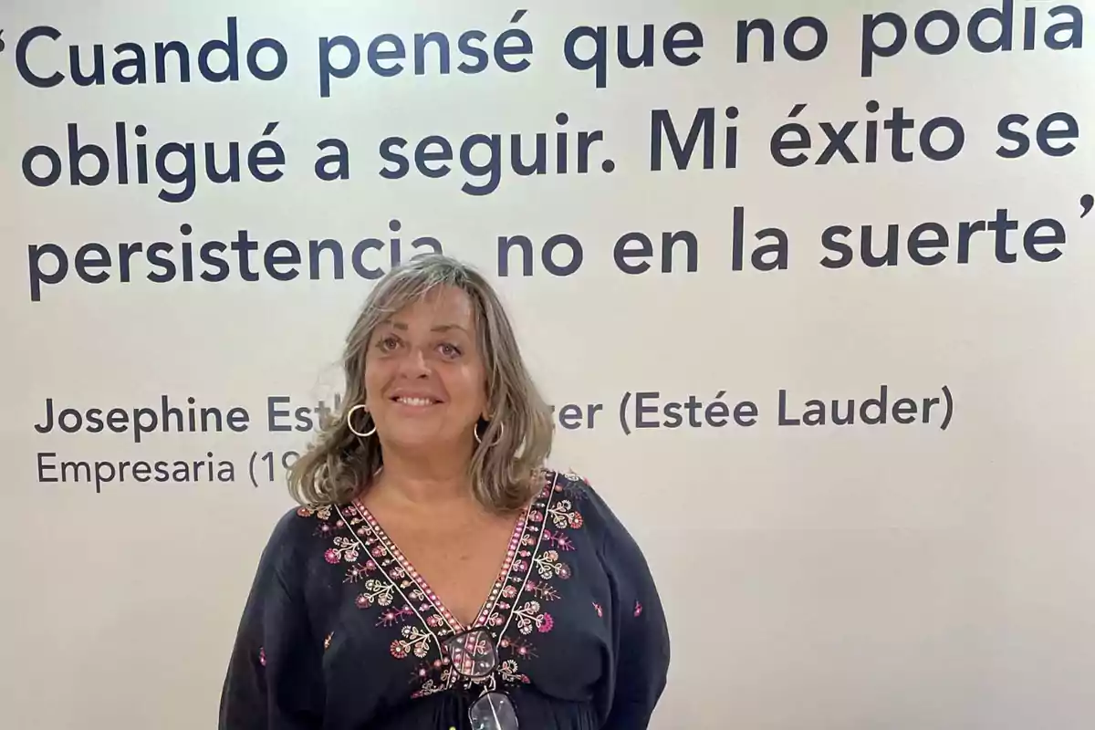 Una mujer sonriente está de pie frente a una pared que tiene una cita inspiradora de Josephine Esther Mentzer (Estée Lauder), una empresaria nacida en 1906.