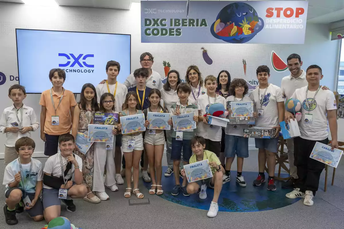 Grupo de niños y adultos posando juntos en un evento de DXC Iberia Codes, algunos sostienen diplomas y premios, con un cartel de fondo que promueve detener el desperdicio alimentario.