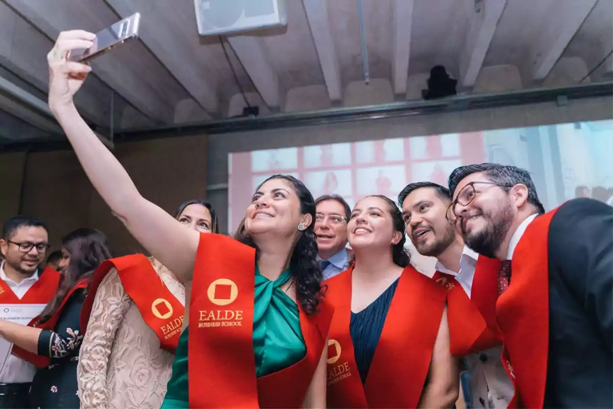 Personas con estolas rojas de EALDE Business School tomándose una selfie en un evento.