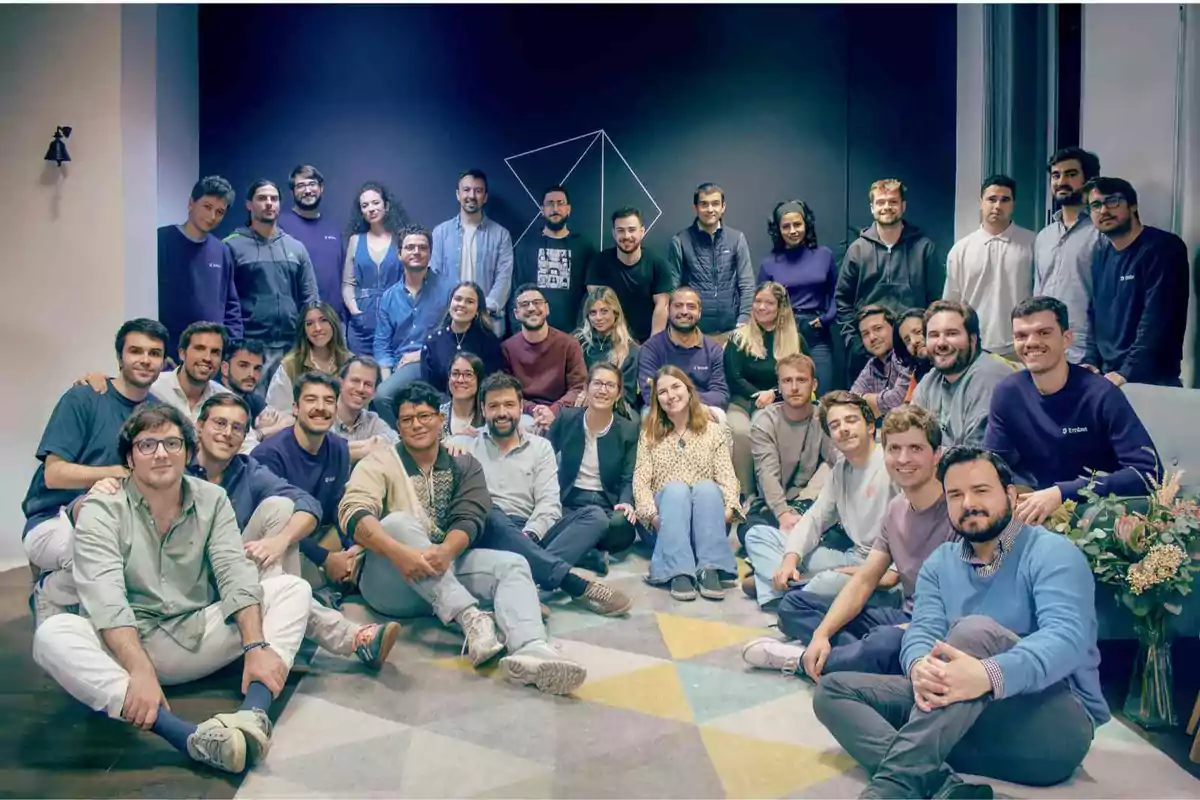 Un grupo de personas posando juntas en una sala con un fondo oscuro y un diseño geométrico en la pared.