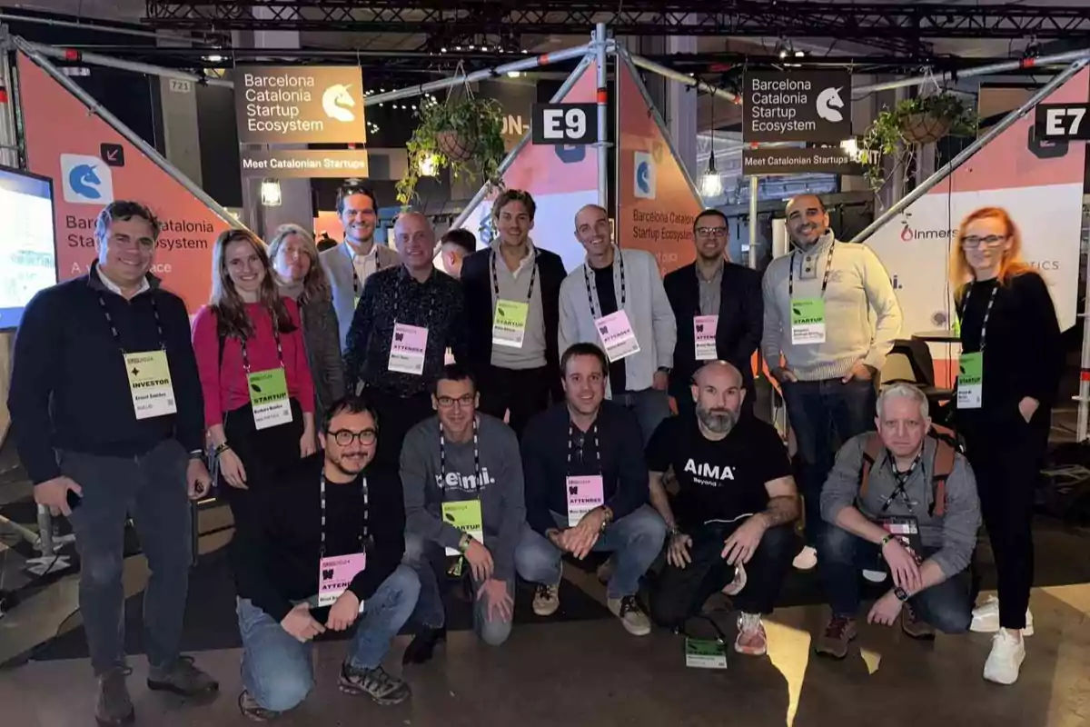 Un grupo de personas posando en un evento de startups en Barcelona, con carteles y credenciales visibles.