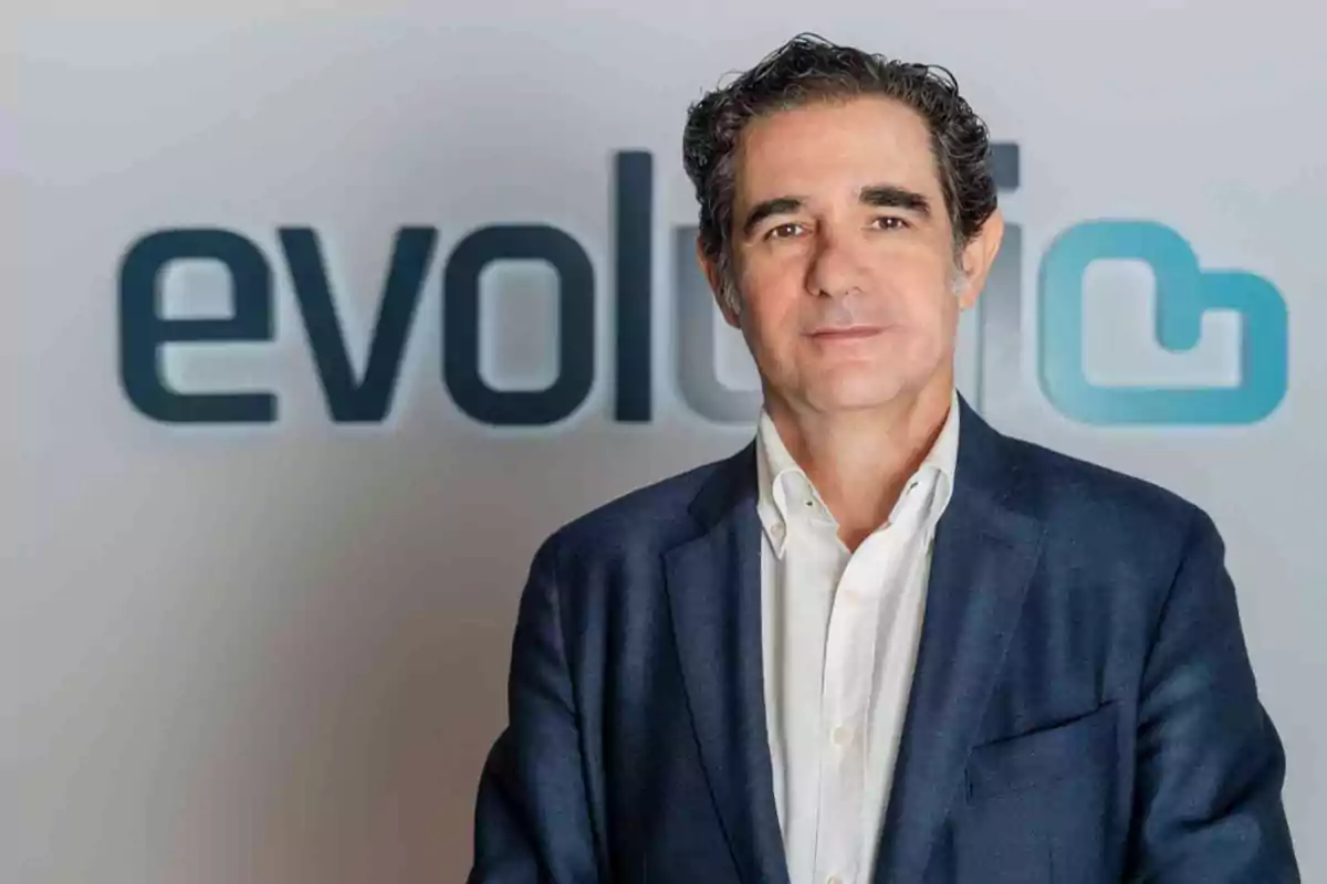 Hombre de cabello oscuro y canoso con saco azul y camisa blanca posando frente a un fondo con el logo de evolutio