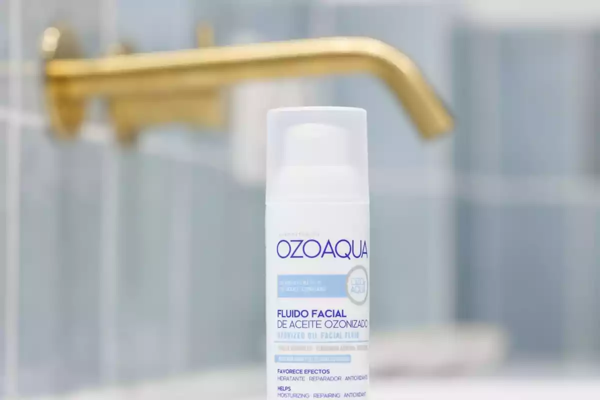 Envase de fluido facial de aceite ozonizado de la marca Ozoaqua en un baño con grifo dorado de fondo.