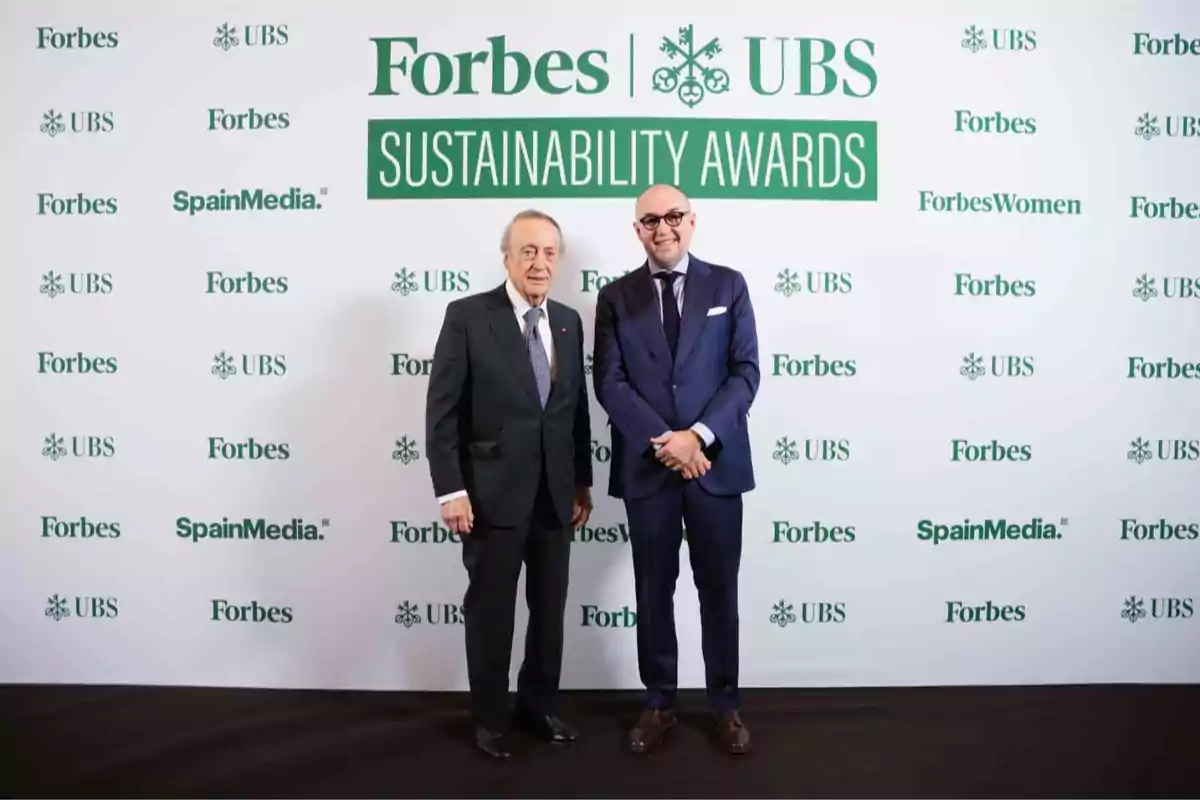 Dos personas posan en un evento de los Forbes UBS Sustainability Awards frente a un fondo con logotipos de Forbes, UBS y SpainMedia.