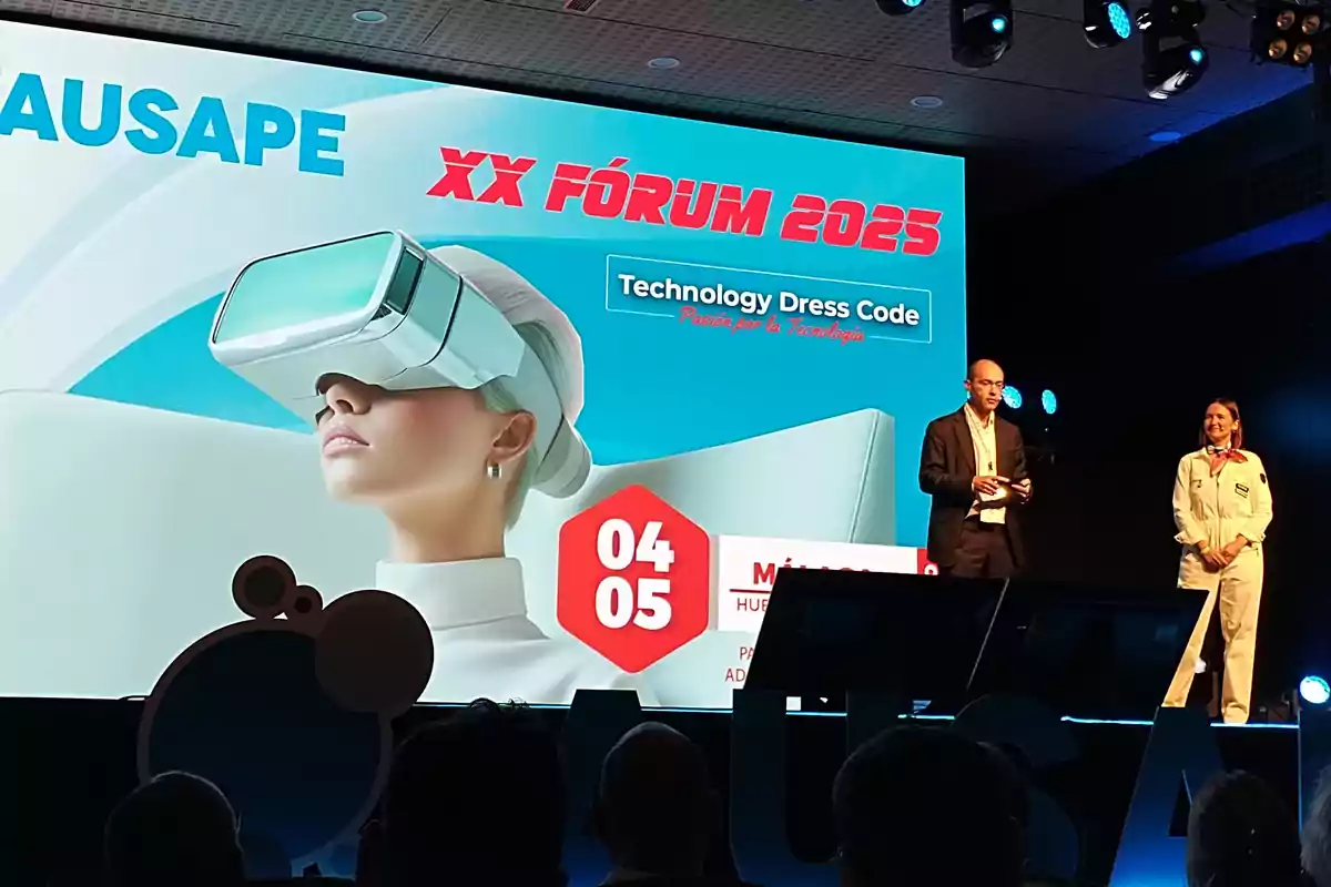 Dos personas en un escenario presentan el XX Fórum 2025 de AUSAPE, con una gran pantalla de fondo que muestra una imagen de una mujer usando gafas de realidad virtual y el lema Technology Dress Code.