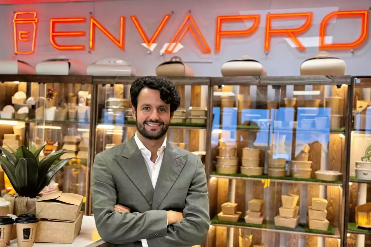 Hombre de traje gris sonriendo frente a un estante con envases y un letrero de neón que dice "ENVAPRO".