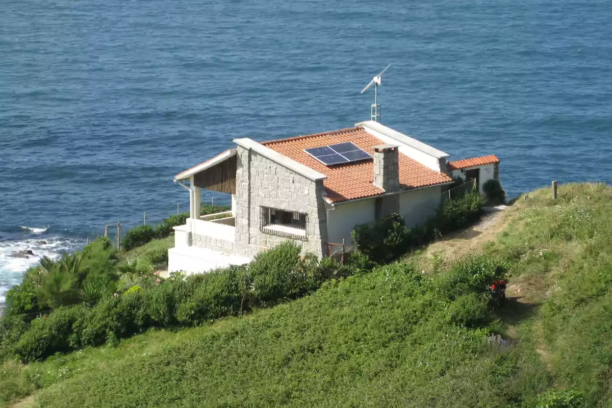 Casa de piedra con techo de tejas y paneles solares ubicada en un acantilado frente al mar.