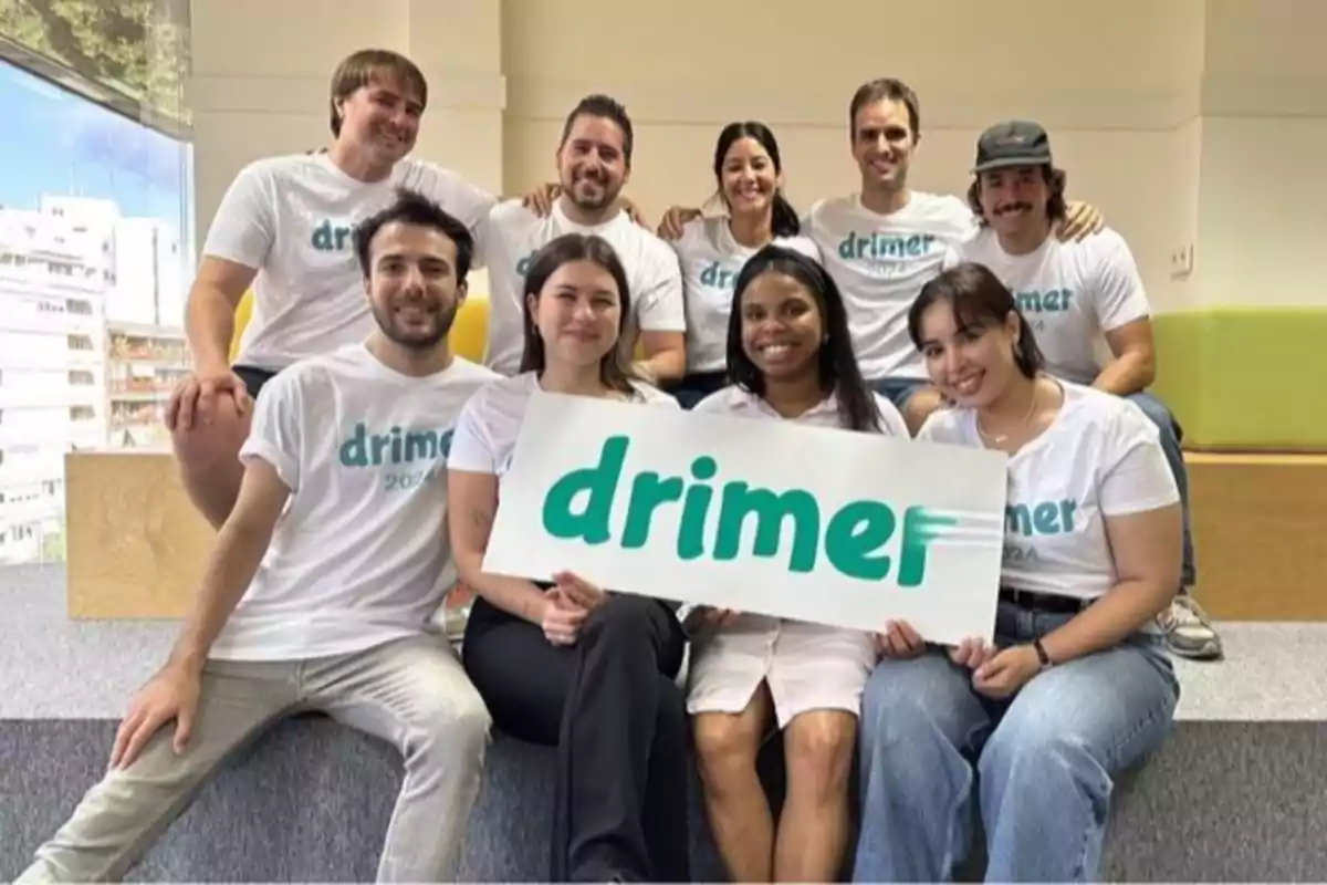 Un grupo de personas sonríe mientras sostiene un cartel con la palabra "drimer" en un entorno interior.