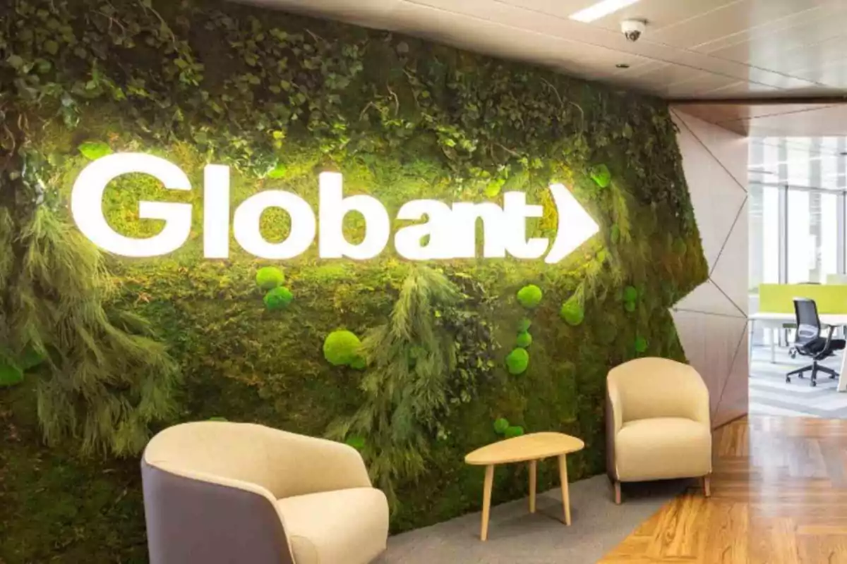 Oficina moderna con pared verde y logo iluminado de Globant junto a dos sillones y una mesa pequeña.
