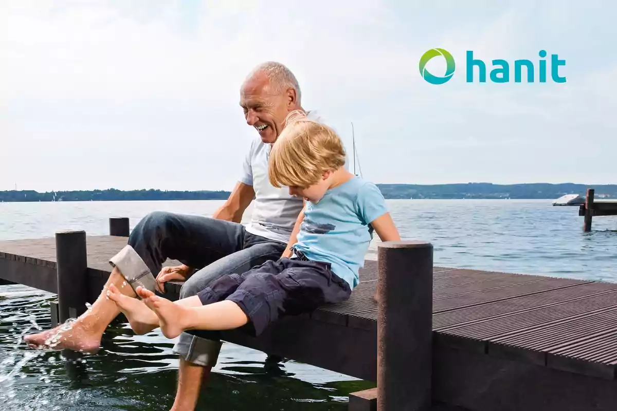 Un hombre mayor y un niño sentados en un muelle disfrutando del agua en un día soleado.