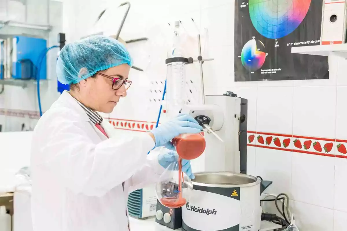 Persona en un laboratorio usando equipo de laboratorio y vertiendo líquido rojo en un matraz.