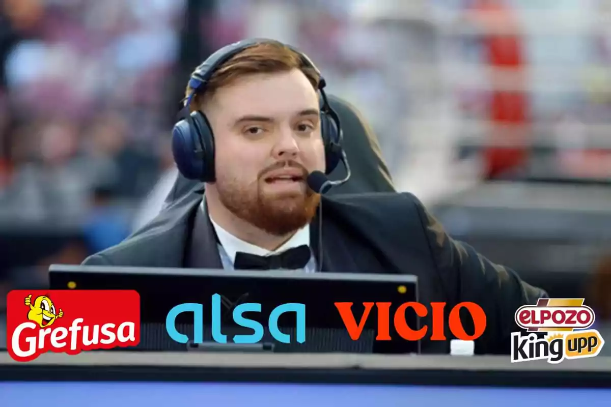 Un hombre con auriculares y micrófono está sentado frente a una mesa con logotipos de varias marcas, incluyendo Grefusa, Alsa, Vicio y El Pozo King. Está vestido con un esmoquin y parece estar en un evento o transmisión en vivo.