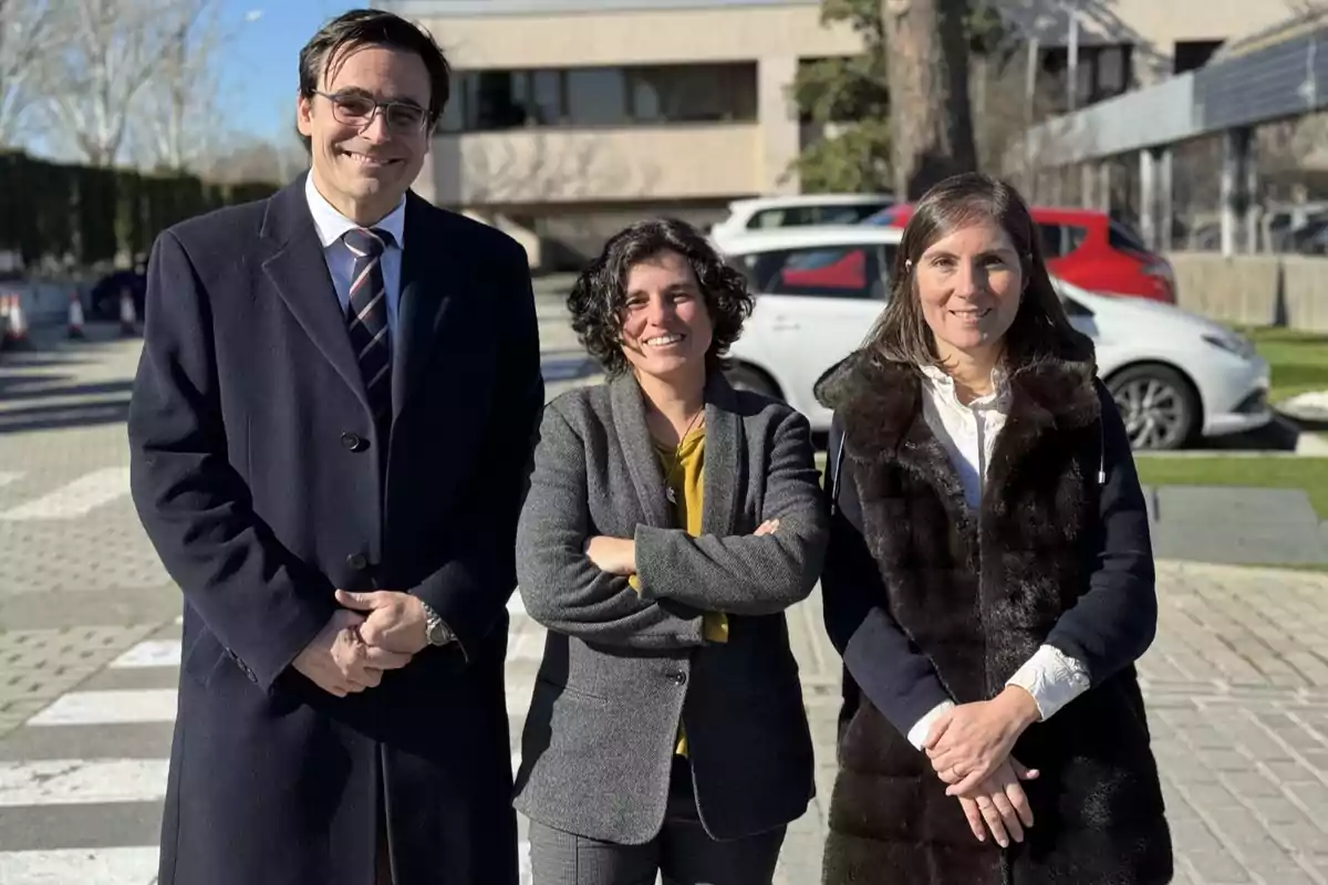 Tres personas posan al aire libre en un entorno urbano, vestidas con ropa de invierno y sonriendo a la cámara.