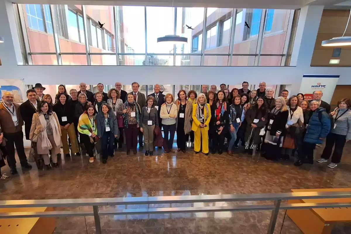 Un grupo grande de personas posando juntas en un espacio interior con ventanas grandes al fondo.