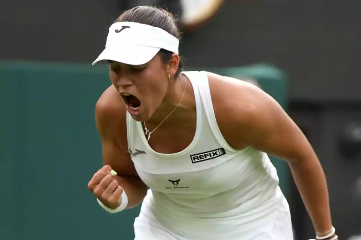 Jugadora de tenis celebrando con emoción durante un partido, vestida con ropa deportiva blanca y una visera blanca.