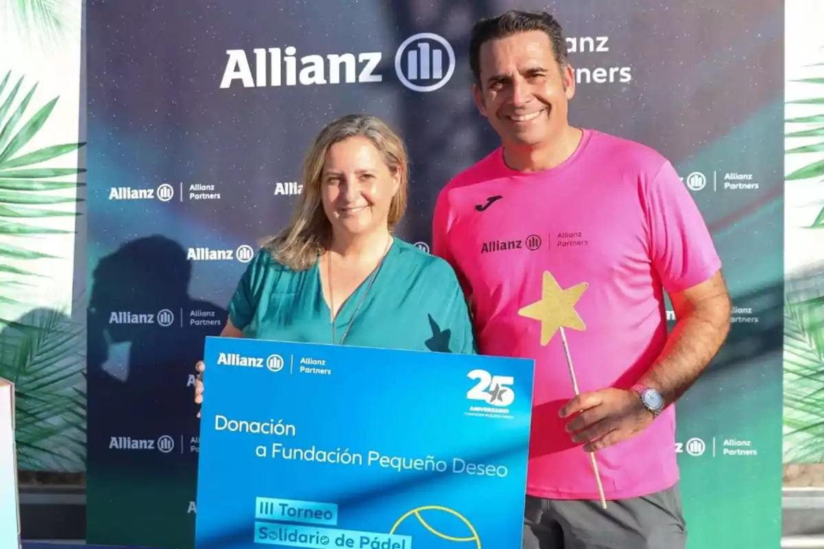 Dos personas sonríen mientras sostienen un cartel de donación a la Fundación Pequeño Deseo en un evento de Allianz Partners, una de ellas lleva una camiseta rosa y sostiene una varita con estrella.