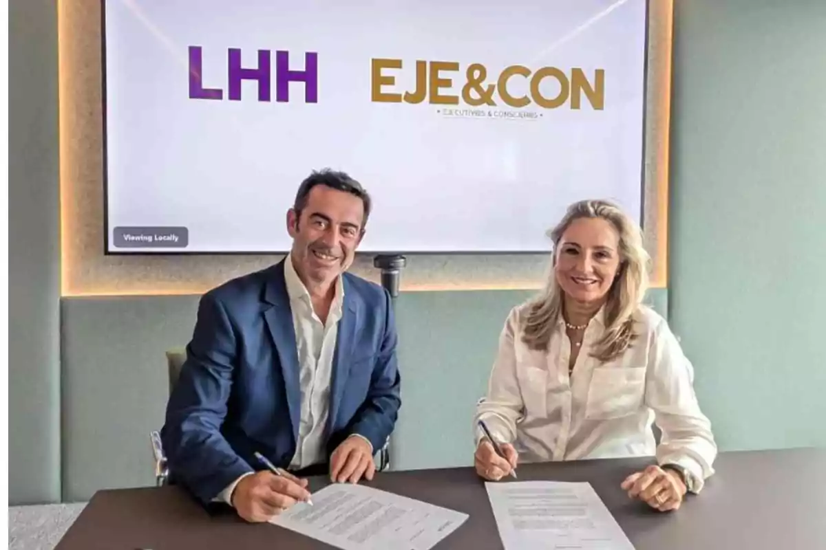 Dos personas sentadas en una mesa firmando documentos con un cartel detrás que dice "LHH EJE&CON".