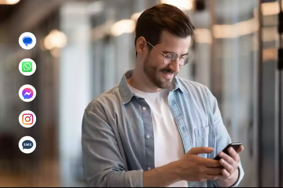 Hombre sonriendo mientras usa su teléfono móvil con iconos de aplicaciones de mensajería a su lado.