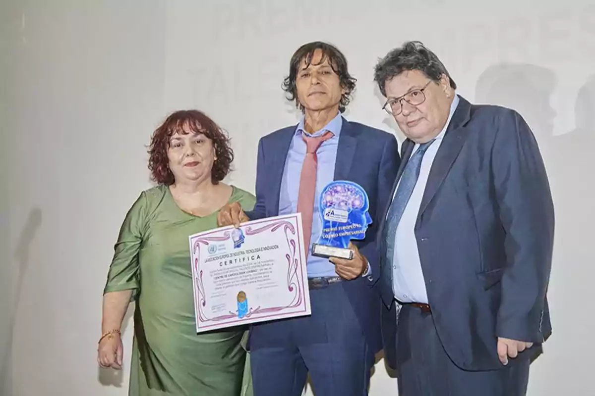 Tres personas posan juntas mientras una de ellas sostiene un certificado y un trofeo.