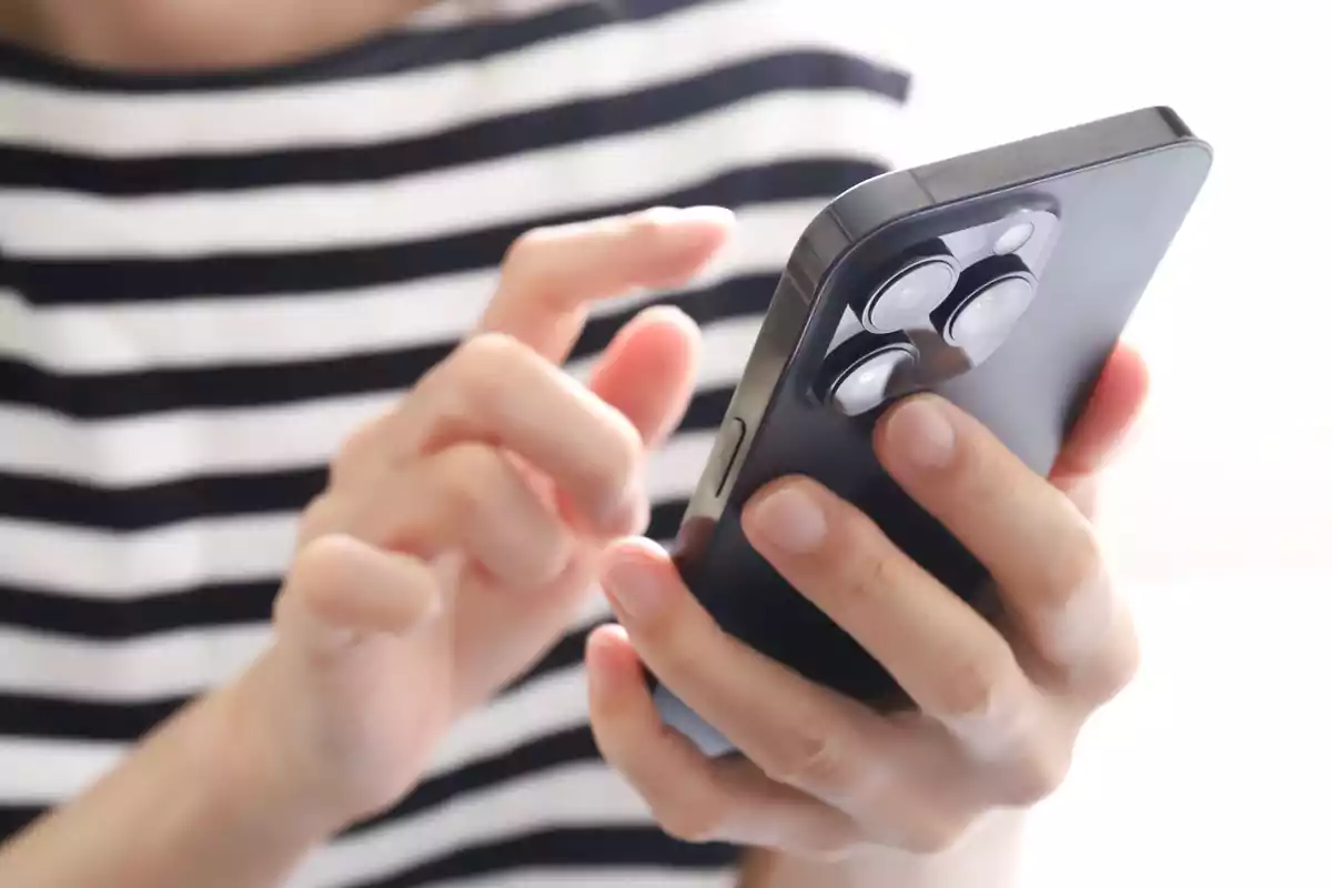 Persona usando un teléfono móvil con una funda negra y una camiseta de rayas.