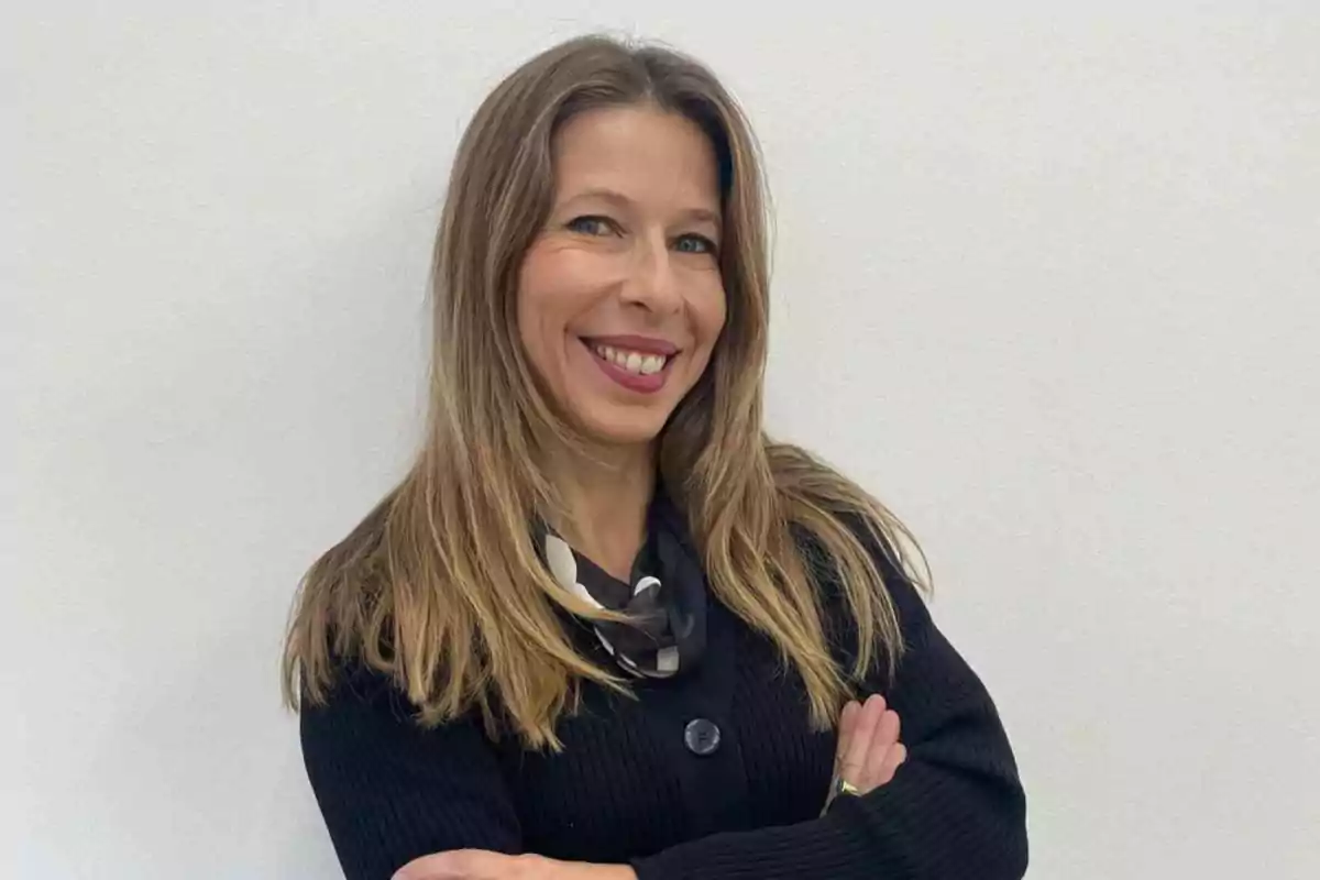 Una mujer sonriendo con los brazos cruzados frente a un fondo blanco.