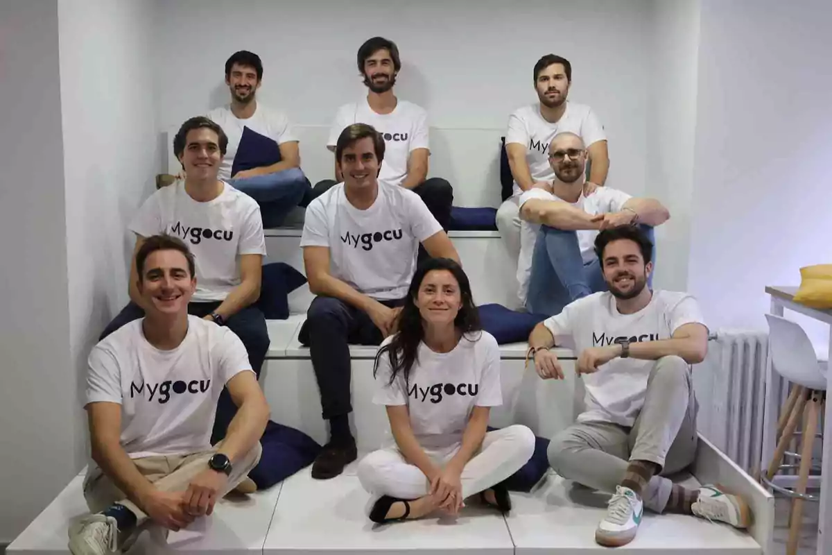 Un grupo de personas sentadas en una estructura escalonada, todas vistiendo camisetas blancas con el logo de "Mygocu".