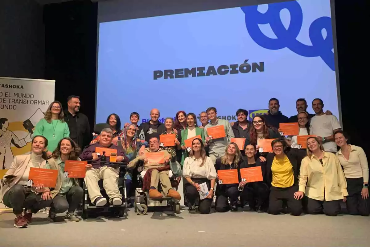 Un grupo de personas sonríe mientras sostiene certificados en un evento de premiación, con un cartel de Ashoka al fondo.