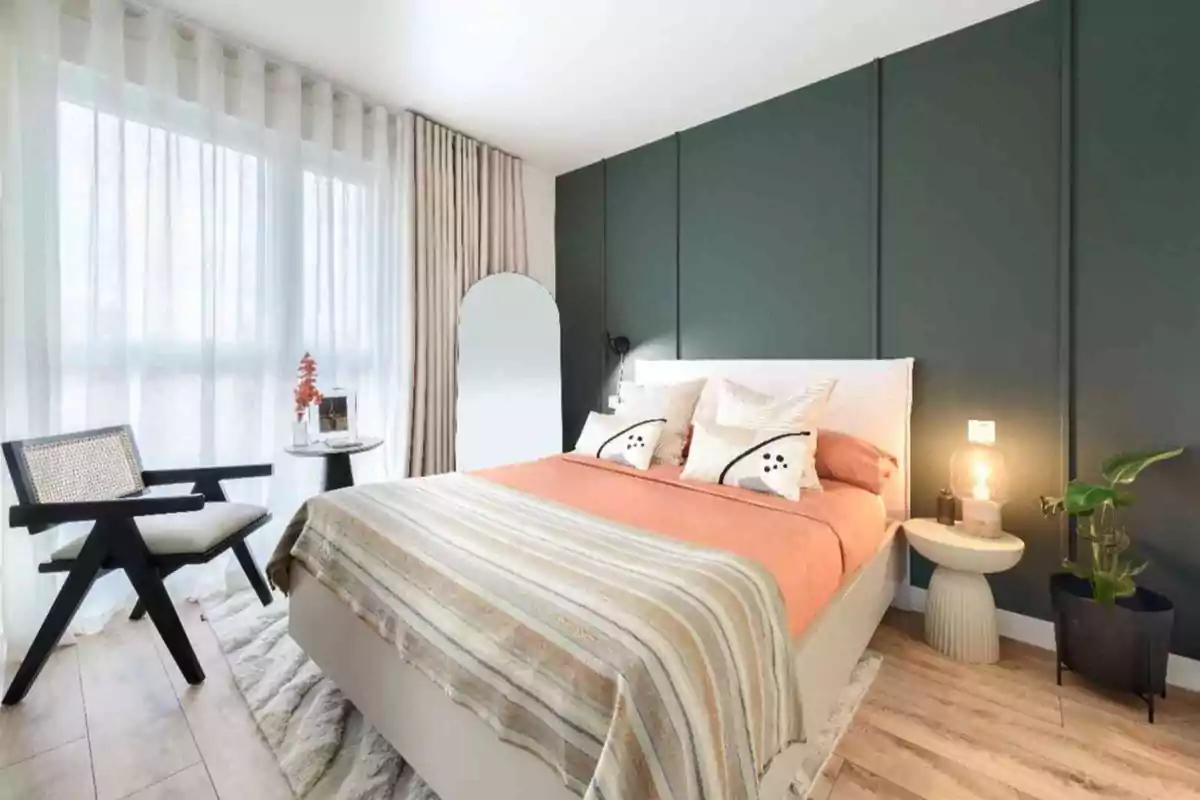 Habitación moderna con cama de sábanas naranjas, cojines decorativos, pared verde oscuro, silla negra, mesa auxiliar con lámpara y planta, y cortinas blancas translúcidas.